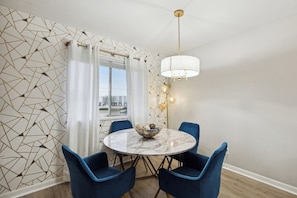 A dining area with a round table, blue chairs, a white marble top, a gold chandelier, and a geometric patterned wall. - The Hangar #11 - 2BR - 1BA (Lansing)