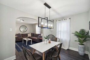 Een moderne woonkamer met een eethoek, een ronde spiegel en een plant in pot.