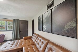 Ein Zimmer mit einem braunen Ledersofa, einem Fenster mit Vorhängen und drei gerahmten Landschaftsbildern an der Wand.