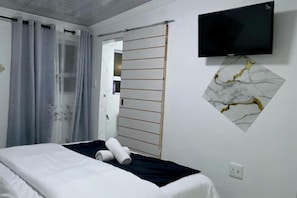 Et hotelværelse med en seng, et fjernsyn monteret på væggen og en skydedør.