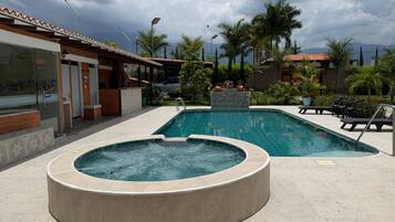 Una piscina con jacuzzi, rodeada de palmeras y un edificio con tejado de baldosas.