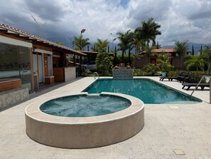Una piscina con jacuzzi, rodeada de palmeras y un edificio con tejado de baldosas.