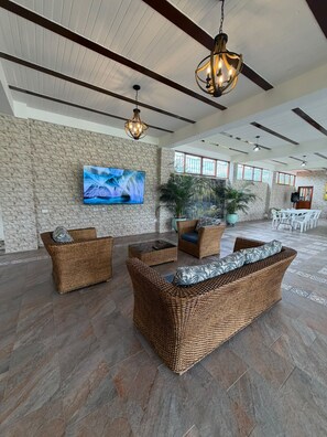 A spacious lobby with a stone wall, a large flat-screen TV, wicker furniture, and a ceiling fan.