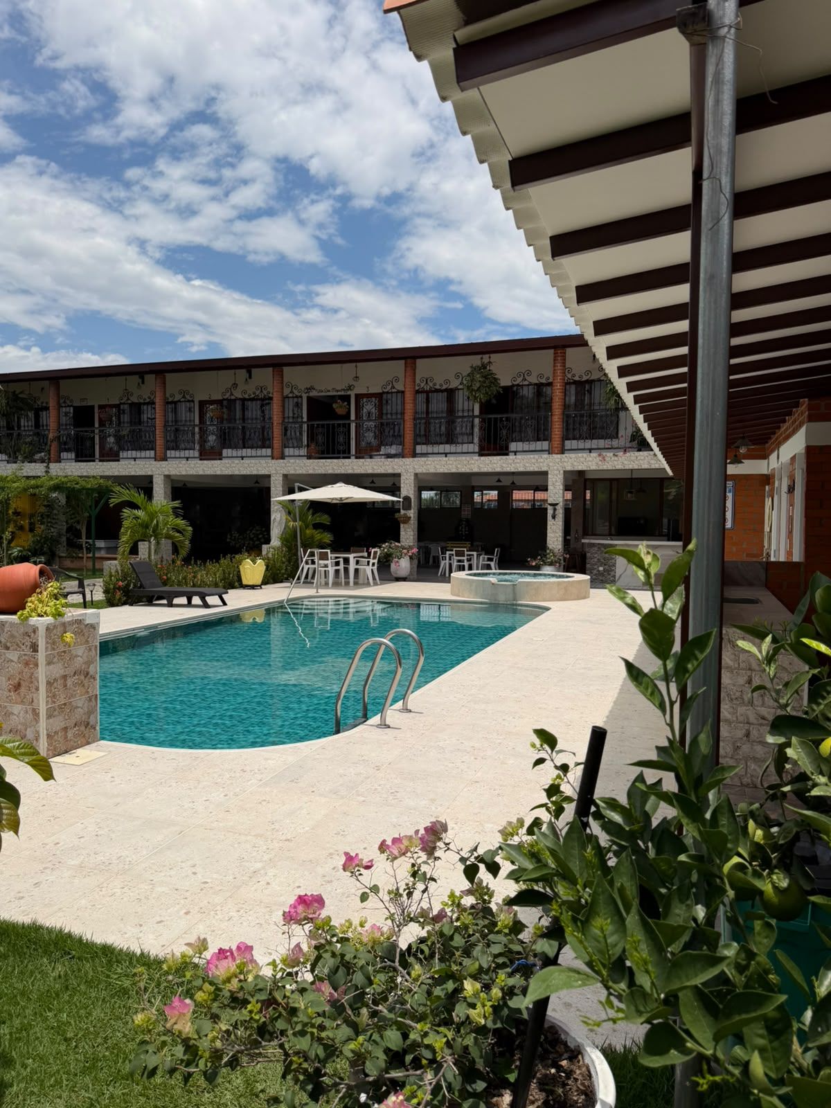 A swimming pool with a sunshade, surrounded by a covered patio area with outdoor seating.