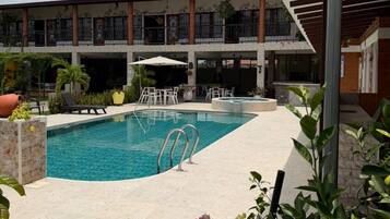 A swimming pool with a sunshade, surrounded by a covered patio area with outdoor seating.