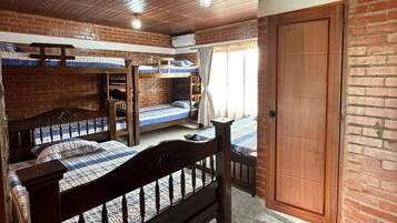 Una habitación con techo de madera, paredes de ladrillo, cama de madera, armario y ventana con cortinas.