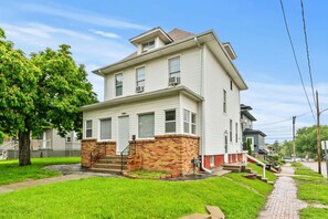 A two-story residential building with a brick foundation and white siding. - Spacious downtown getaway for the whole family! (Omaha)