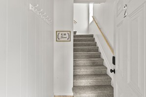 A staircase with a grey carpet, a wooden handrail, and a door with a black handle. - Spacious downtown getaway for the whole family! (Omaha)