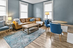 A living room with a brown leather sofa, a wooden coffee table, a blue armchair, and a small round table with a lamp. - Spacious downtown getaway for the whole family! (Omaha)