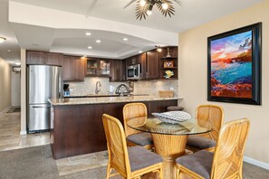 A modern kitchen with dark wood cabinets, a stainless steel refrigerator, and a glass island with seating. - South Kihei condo with partial ocean view, pool, hot tub, and lanai (Kihei)