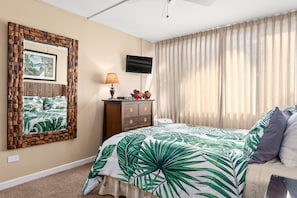 A hotel room with a bed, a television, a desk with a lamp, and a wall-mounted picture. - South Kihei 1BR condo with partial ocean view, pool, hot tub, and lanai (KS5311) (Kihei)