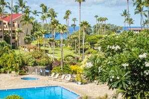 A pool area with lounge chairs, a pool, and a view of palm trees and a building. - South Kihei 1BR condo with partial ocean view, pool, hot tub, and lanai (KS5311) (Kihei)