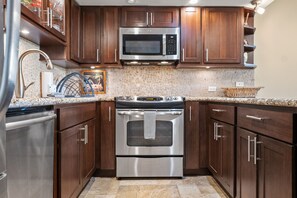 A kitchen with stainless steel appliances, wooden cabinets, a granite countertop, and a stone backsplash. - South Kihei 1BR condo with partial ocean view, pool, hot tub, and lanai (KS5311) (Kihei)