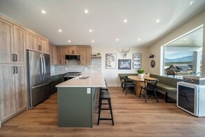 A modern kitchen with wooden cabinets, stainless steel appliances, a central island, and a dining area with a view.