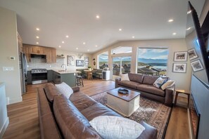 A spacious living area with a brown leather sofa, a coffee table, and a view of mountains through large windows.