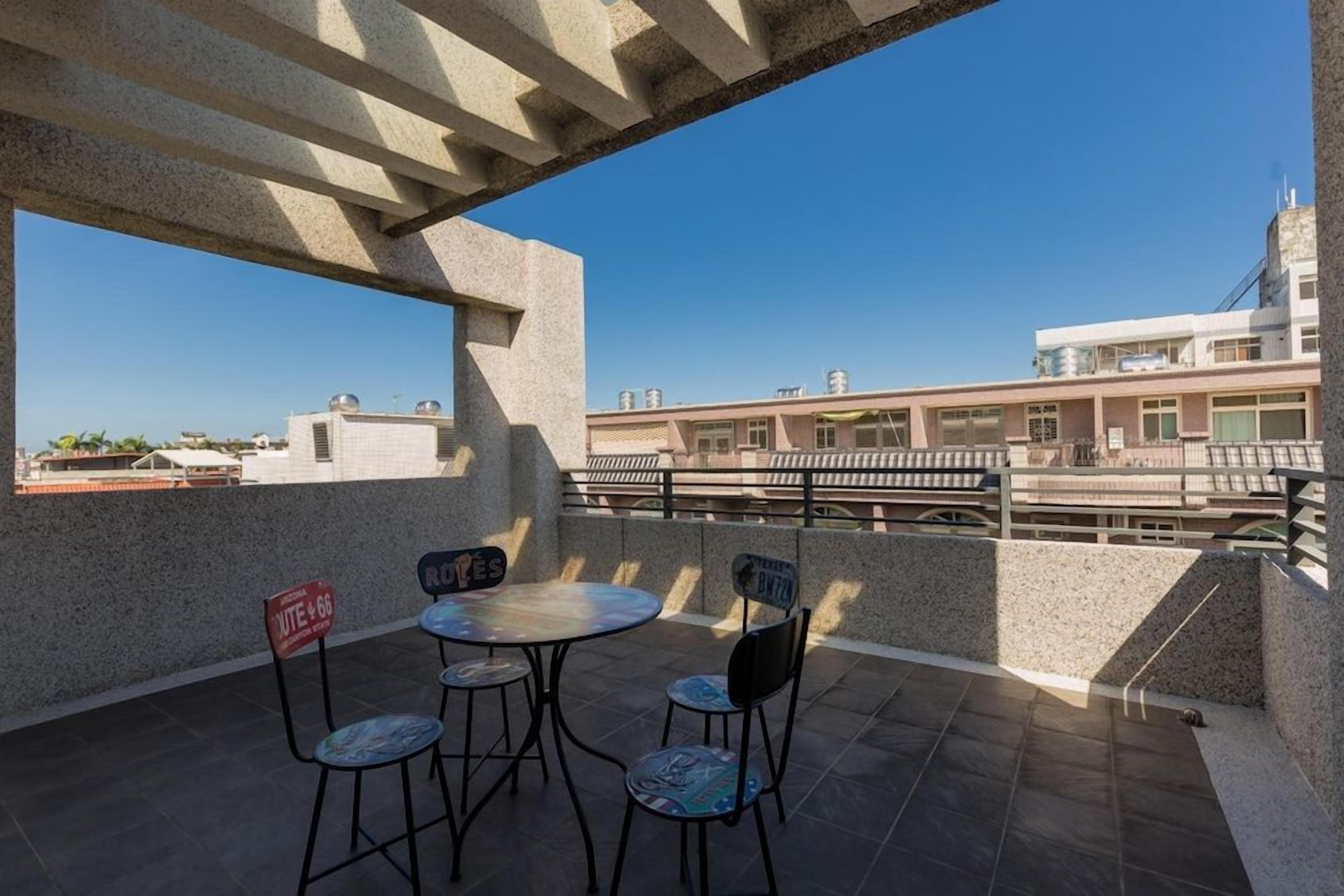Eine Außenpatio mit einem runden Tisch und vier Stühlen, einer Betonkonstruktion darüber und Blick auf Gebäude im Hintergrund.