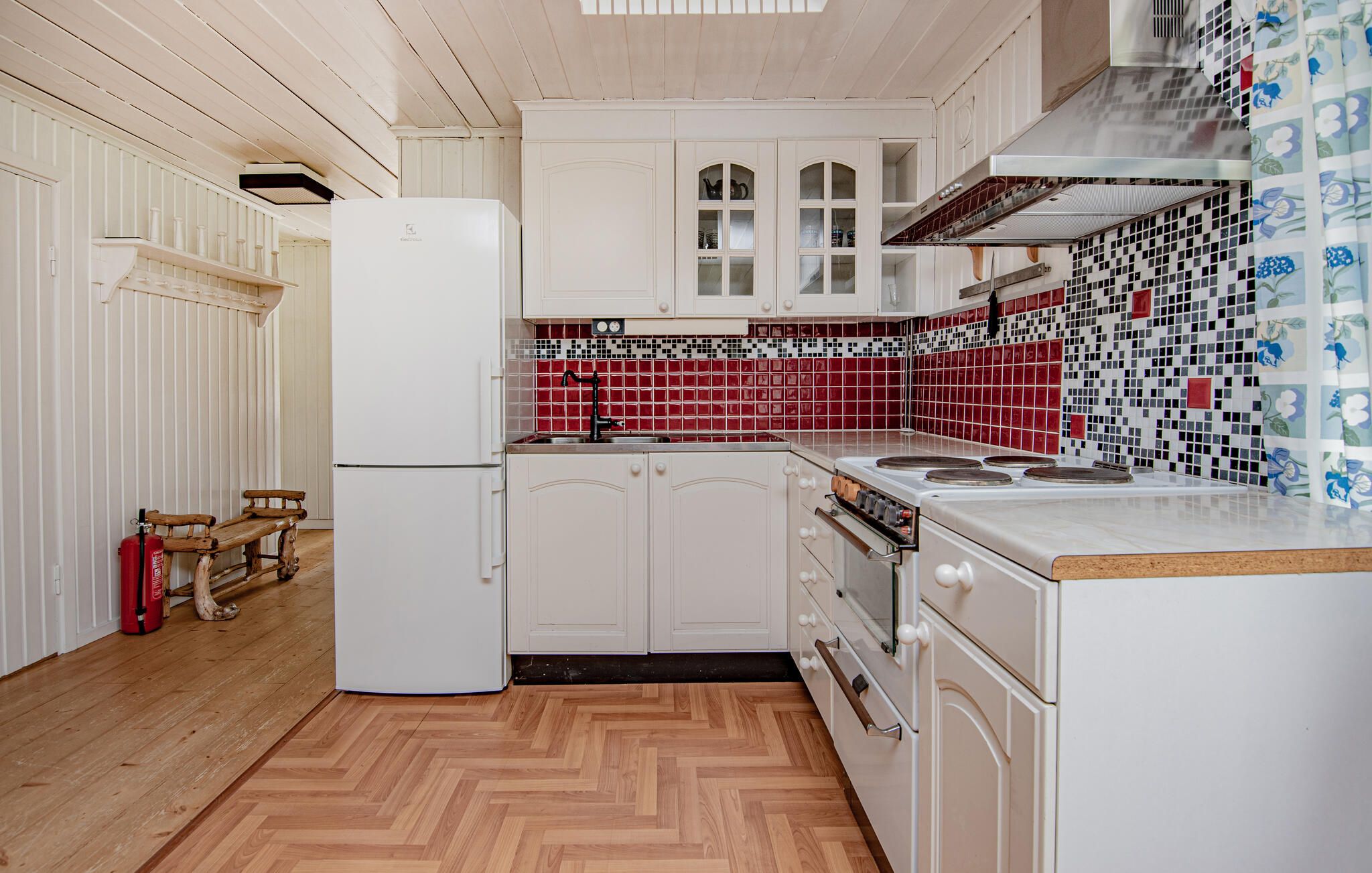 Une cuisine avec des meubles blancs, un crédence carrelé de carreaux rouges, un réfrigérateur blanc et un plancher en bois.