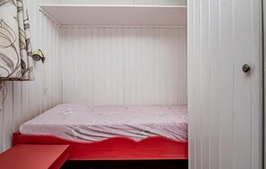 A small, single-bed room with a red bench, white walls, and a door. - Amazing home in Tärnaby with sauna (Tärnaby)