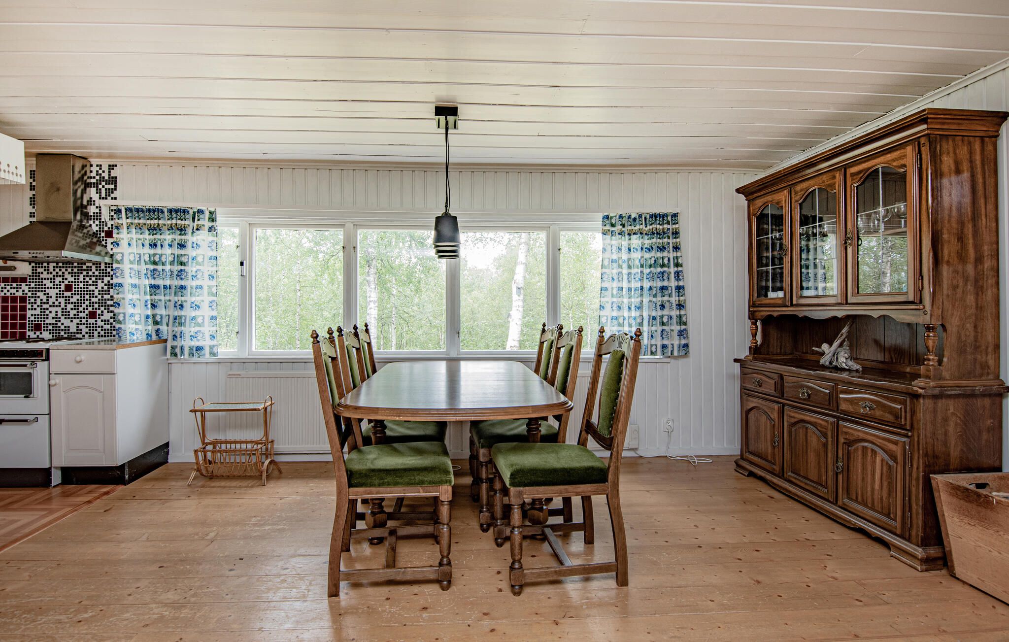 Une salle à manger avec une table et des chaises en bois, un coin cuisine avec un fourneau et un grand buffet en bois.
