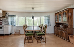A dining room with a wooden table and chairs, a kitchen area with a stove, and a large wooden cabinet. - Amazing home in Tärnaby with sauna (Tärnaby)