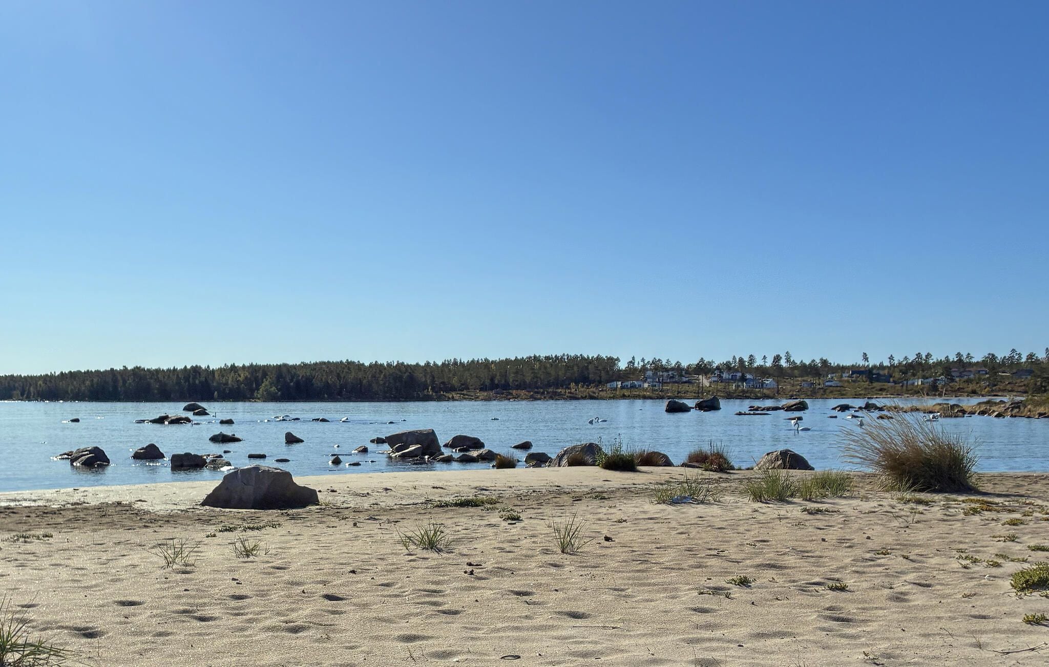 A beach with sand, rocks, and a calm body of water.