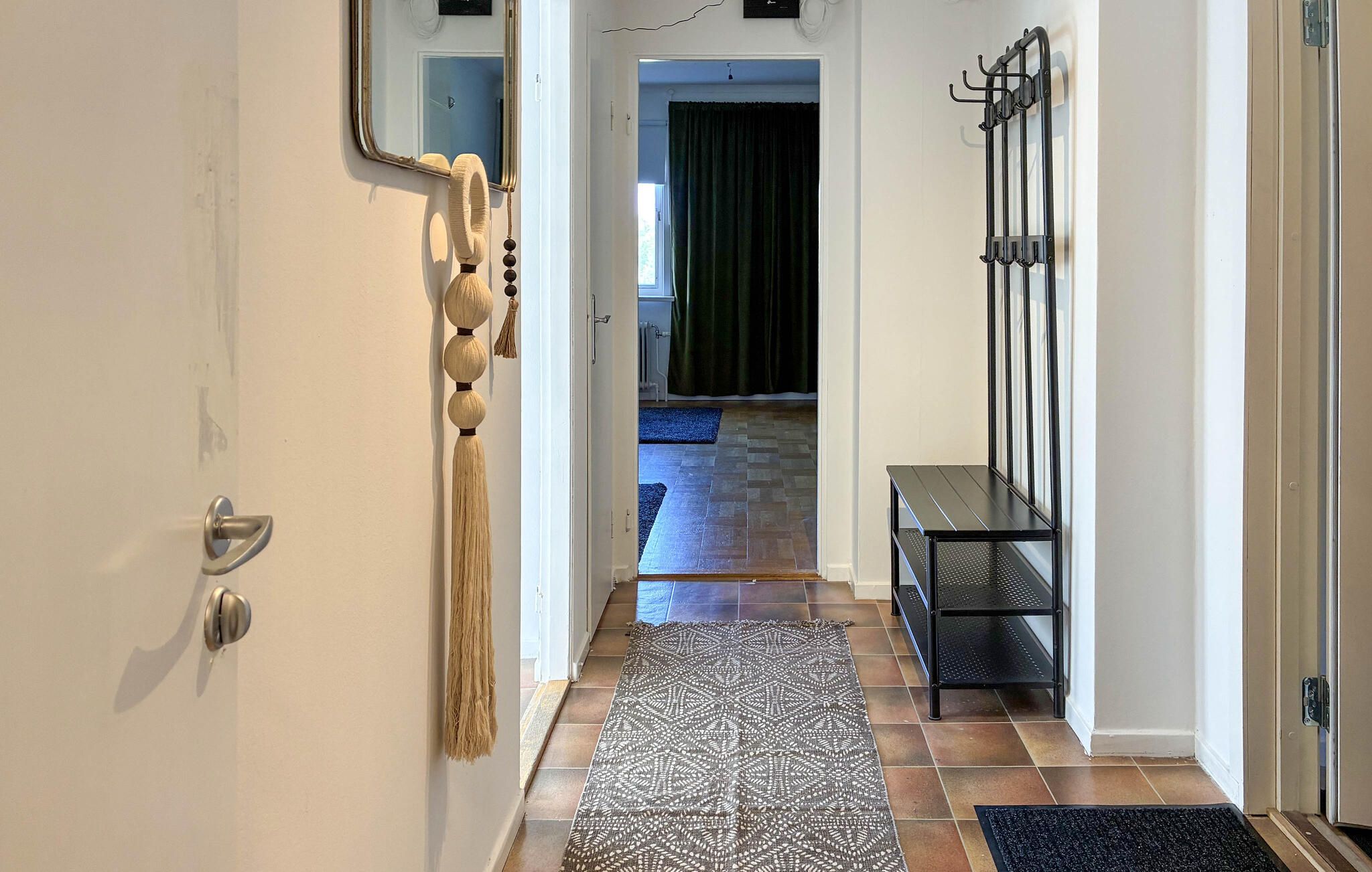 A hallway with a patterned rug, a coat rack, and a door with a mirror.