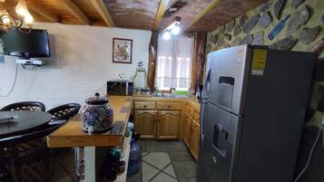 Een keuken met een stenen muur, houten keukenkastjes, een koelkast en een eettafel met stoelen.
