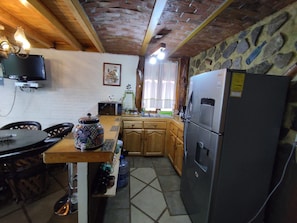 Een keuken met een stenen muur, houten keukenkastjes, een koelkast en een eettafel met stoelen.