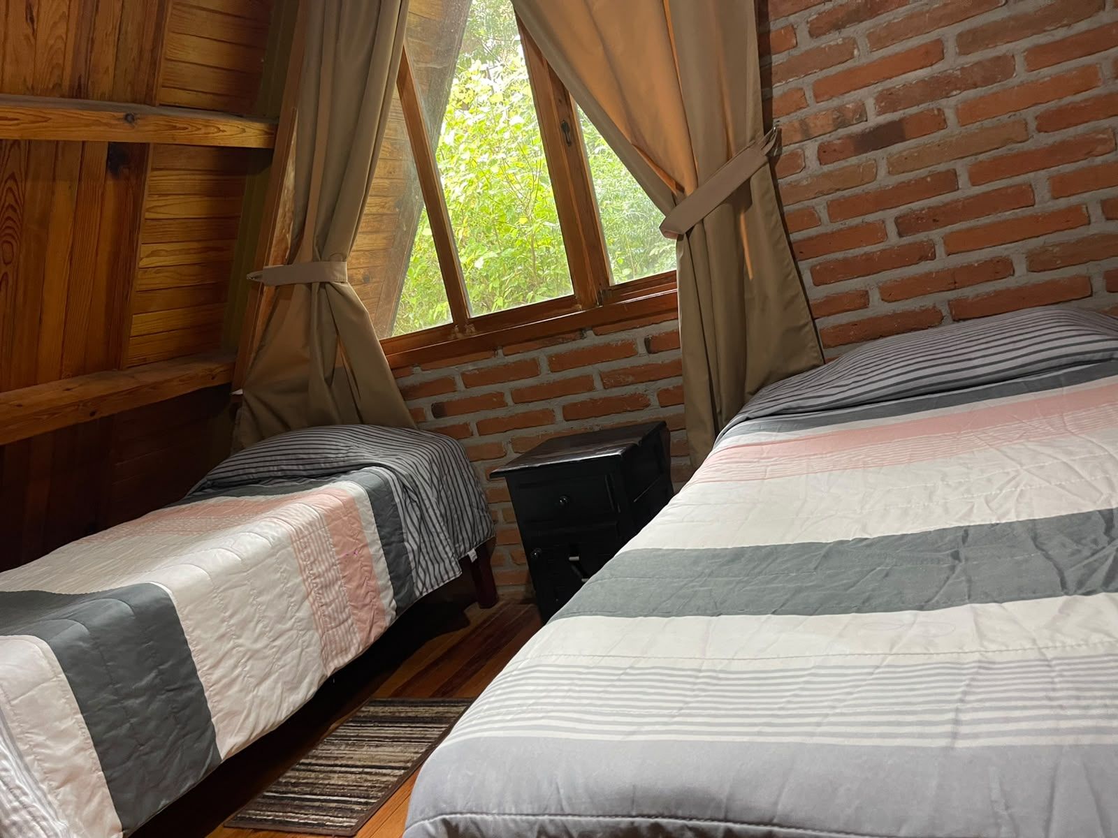 Een kamer met twee bedden, houten wanden, een raam met gordijnen en een kleine tafel.