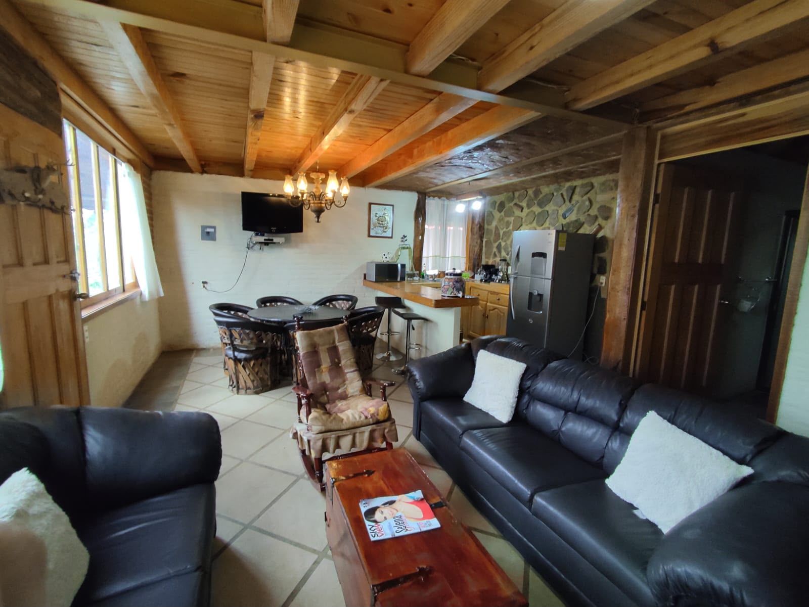 Ein gemütliches Wohnzimmer mit einer schwarzen Ledersofa, einem Holztisch und einem Essbereich mit einem runden Tisch und Stühlen.