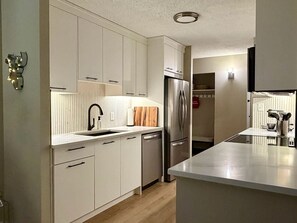 A modern kitchen with white cabinetry, stainless steel appliances, and a central island. - Updated City 2BR | BMO, Saddledome, 17 | Parking (Calgary)