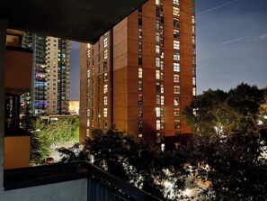 A high-rise building with multiple floors and windows, surrounded by trees and a street with vehicles. - Updated City 2BR | BMO, Saddledome, 17 | Parking (Calgary)