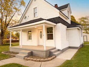 A two-story house with a covered porch, a front door, and a small front yard. - Porchlight Cottage - South Bend, IN (South Bend)