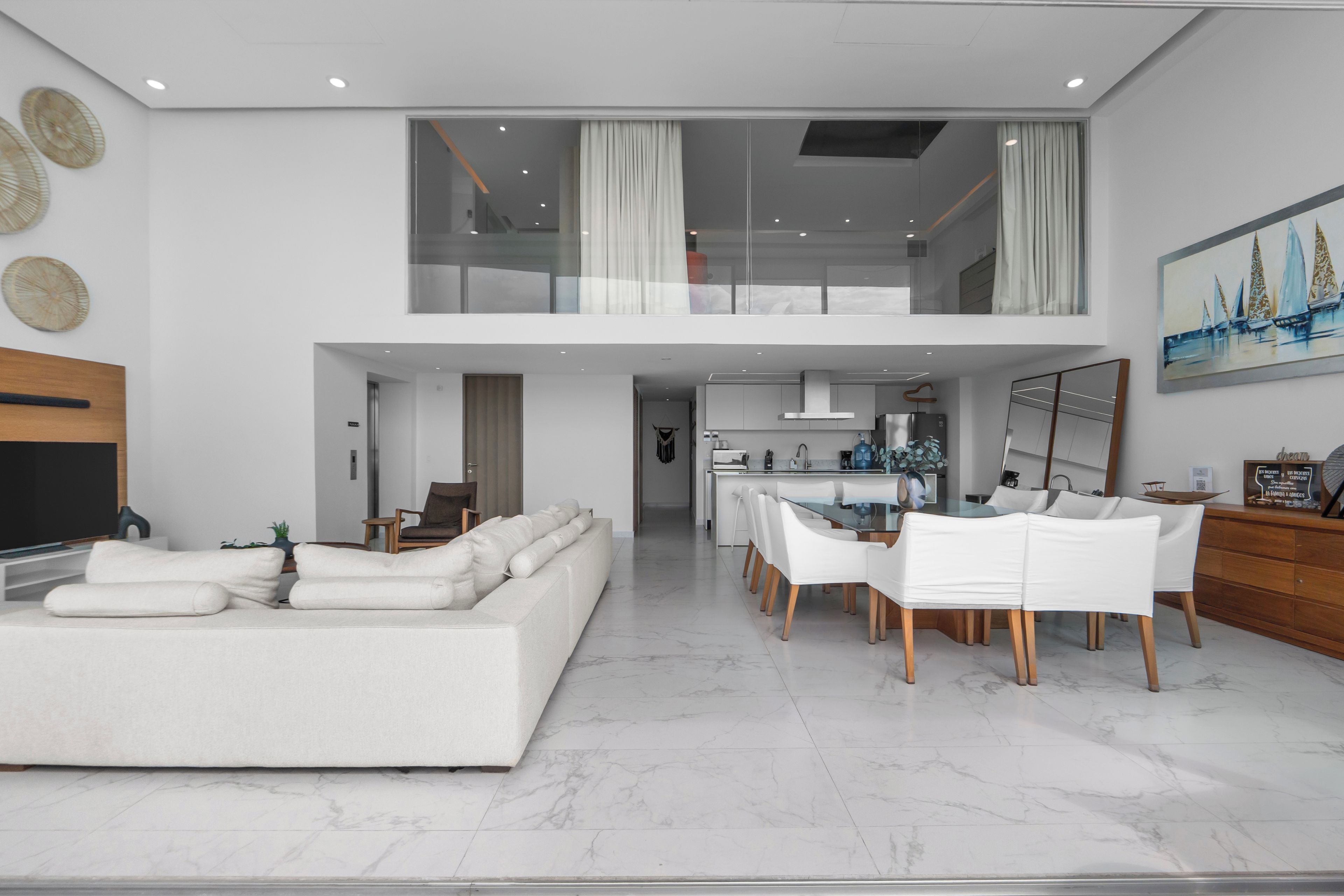 Een moderne woonkamer met een grote bank, een eethoek met witte stoelen, en een keuken op de achtergrond.