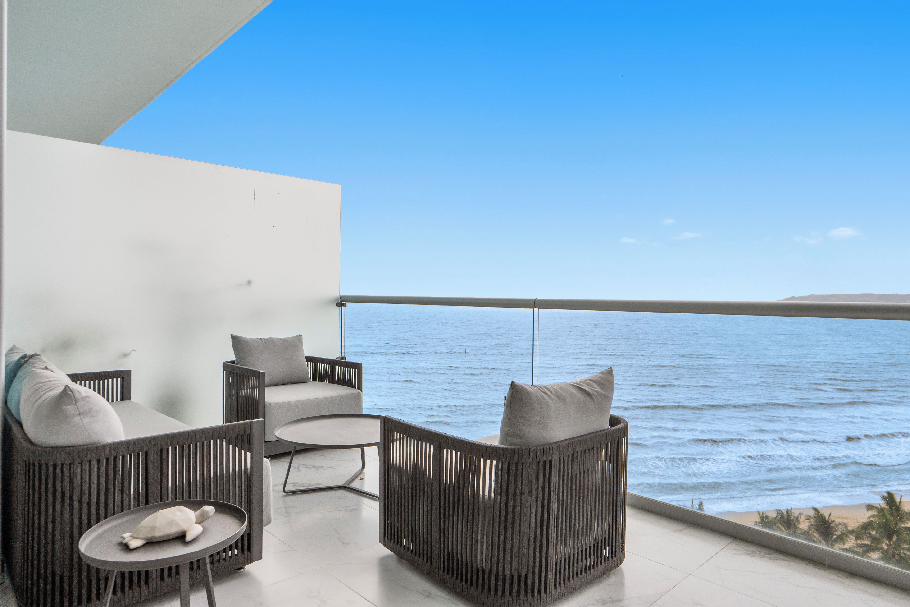 Een balkon met rieten meubels, een kleine ronde tafel en uitzicht op zee.