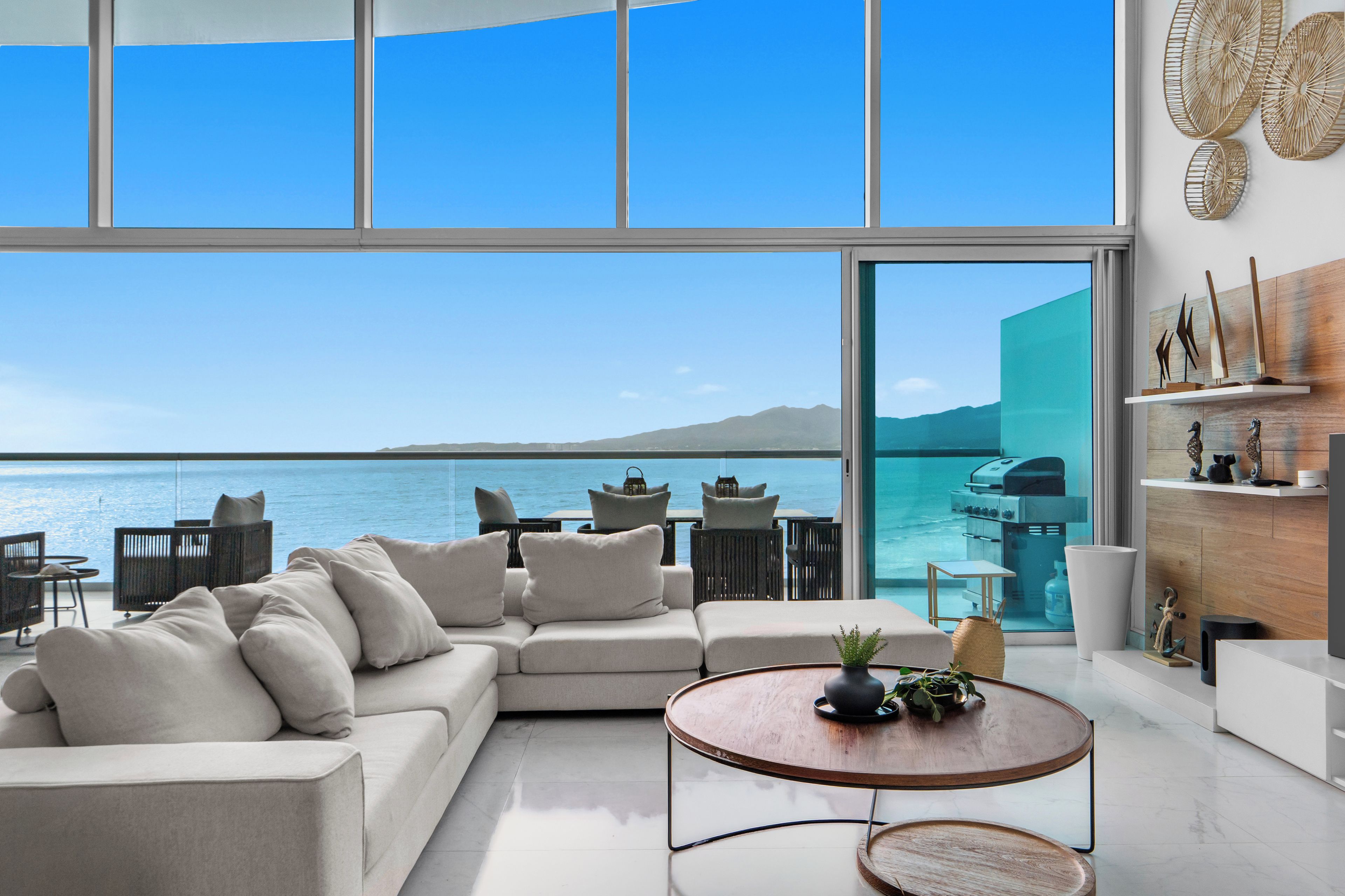 A modern living room with a large window overlooking a body of water and mountains.
