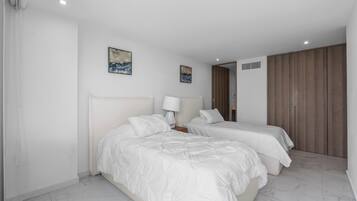 A hotel room with two beds, a nightstand, a lamp, and two paintings on the wall.