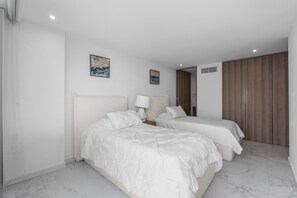 Quarto de hotel com duas camas, uma mesa de cabeceira, uma luminária e duas pinturas na parede.