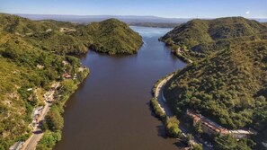 A river winding through a valley with hills on either side, surrounded by greenery and a few buildings. - EL BUHO DEPARTAMENTOS (Villa Carlos Paz)