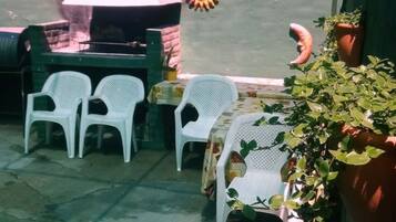 An outdoor seating area with white plastic chairs and tables, a grill, and a potted plant.