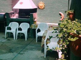 Un espacio exterior con asientos y mesas de plástico blanco, una parrilla y una planta en maceta.