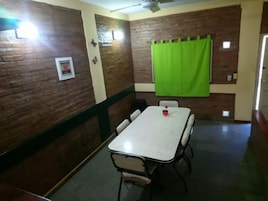 Un salón de conferencias con una mesa blanca, cuatro sillas, una cortina verde y un ventilador de techo.