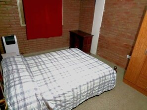 A bedroom with a bed, a red wall, a wooden cabinet, and a white radiator. - EL BUHO DEPARTAMENTOS (Villa Carlos Paz)