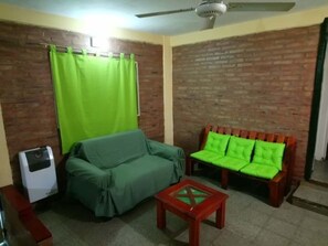 A living room with a green sofa, a wooden bench with green cushions, and a small table. - EL BUHO DEPARTAMENTOS (Villa Carlos Paz)