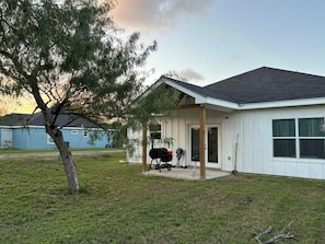 A single-story house with a covered porch, a barbecue grill, and a tree in the foreground. - Private Room with workspace, bathroom, and kitchen. (Harlingen)