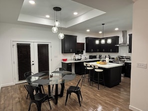 A modern kitchen with dark cabinets, a central island, and a dining area with a glass table and chairs. - Private Room with workspace, bathroom, and kitchen. (Harlingen)