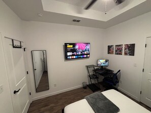 A bedroom with a bed, a desk with a computer, a TV mounted on the wall, and a mirror. - Private Room with workspace, bathroom, and kitchen. (Harlingen)