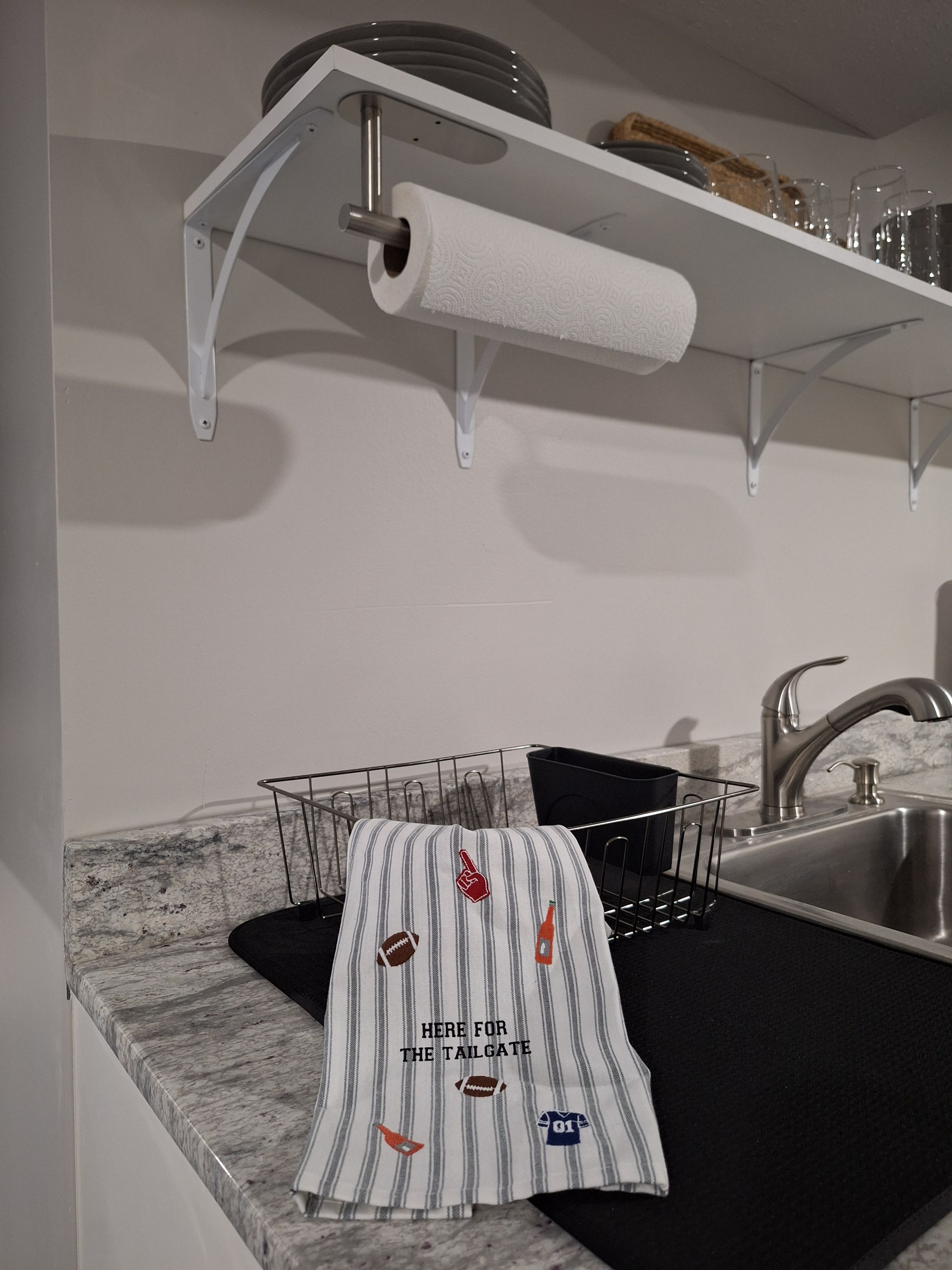 A kitchen with a marble countertop, a stainless steel sink, a towel rack with a striped towel, and a shelf with plates and glasses.