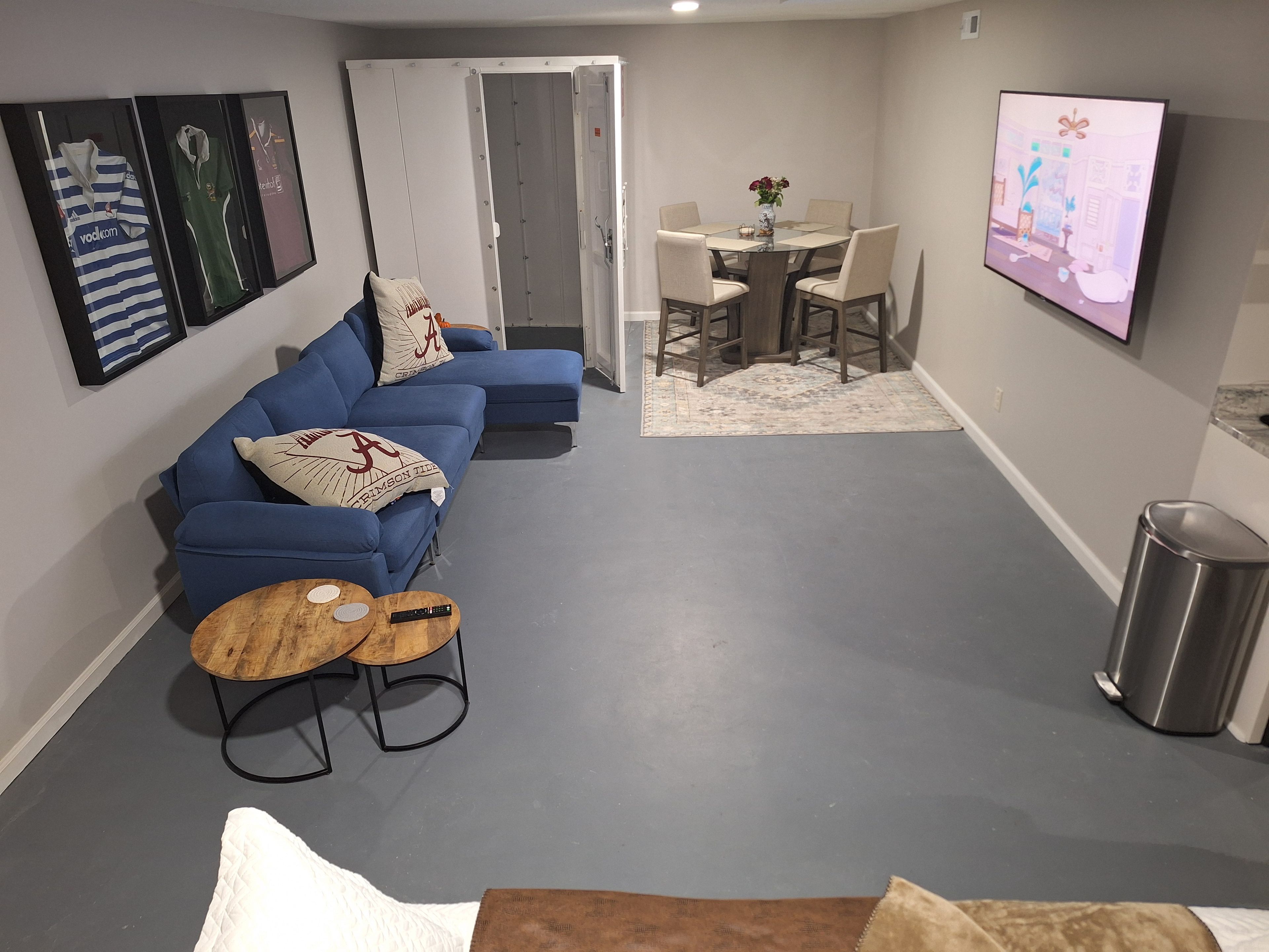 A living room with a blue sofa, a coffee table, and a TV. There is a dining area with a table and chairs.
