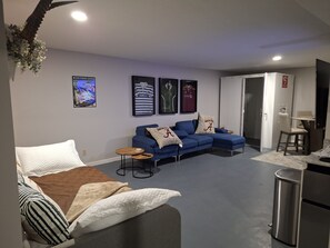 A modern living room with a sectional sofa, a small coffee table, and a TV mounted on the wall. - Lovely unit with waterfront views on Northwood lake in charming Northport (Northport)